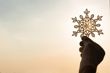 Female hands in a knitted gloves with sparkling huge snowflake on a sunset sky background. Winter and Christmas concept.