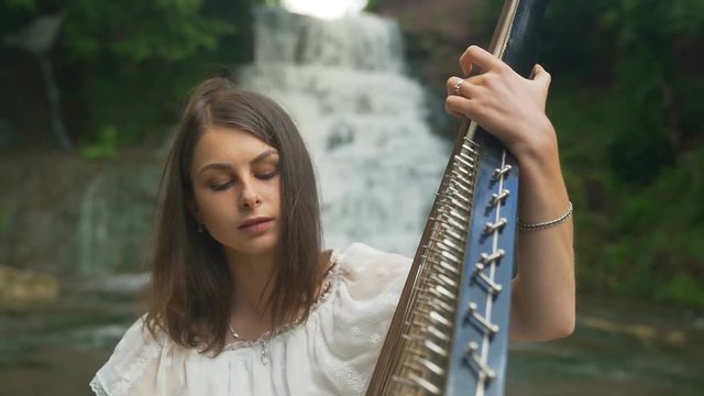 The female hand gently touches the strings of the bandura at waterfall