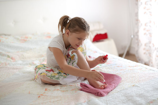 Toddler paints nails on bed, real light interior