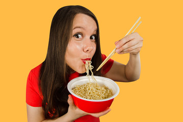 Young girl in a red t-shirt eats chinese noodles with chopsticks isolated on a orange background.