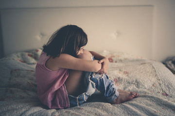 Girl child serious and frustrated sitting on bed