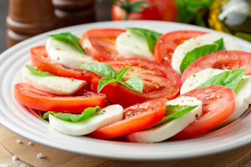 Italian caprese salad with tomatoes, mozzarella cheese and basil in plate on dark wooden background