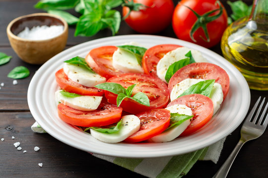 Italian caprese salad with tomatoes, mozzarella cheese and basil in plate on dark wooden background