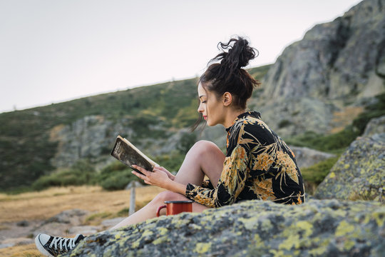 Woman reading book on stone while traveling