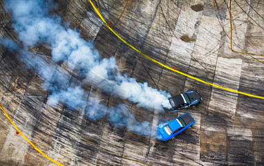 Aerial view from drone. Sport car wheel battle drifting. Blurred of image diffusion race battle drift car with lots of smoke from burning tires on speed track. - obrazy, fototapety, plakaty