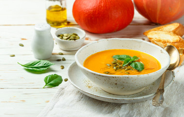 Dietary vegetarian pumpkin cream soup puree with olive oil, seeds and Basil on a light wooden table in a white plate