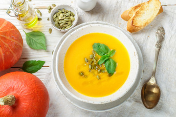 Dietary vegetarian pumpkin cream soup puree with olive oil, seeds and Basil on a light wooden table in a white plate