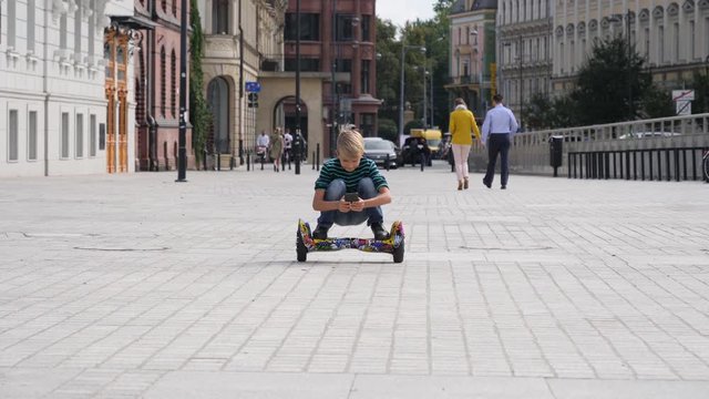 Riding squat on a gyroboard child boy type using his smartphone in a city
