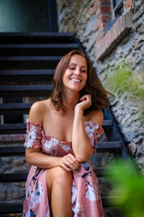 Naklejka premium Young woman in summer dress is sitting on the stairs of a farmhouse