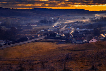 Fototapeta na wymiar Beautiful rural scene with a village in a valley surrounded by smoke from the horns and fog during the winter
