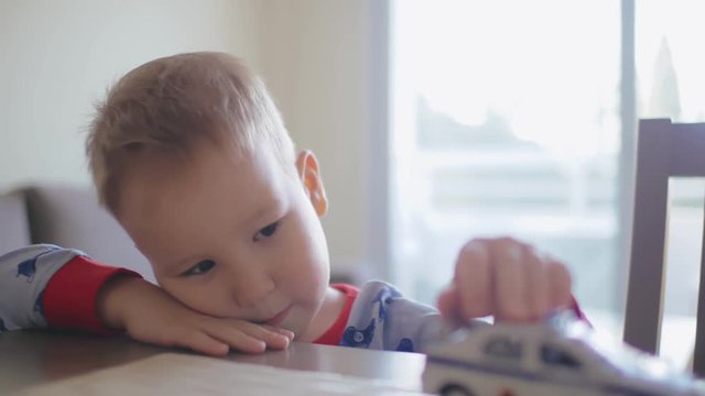 Sad lonely little boy playing with toy car on the table