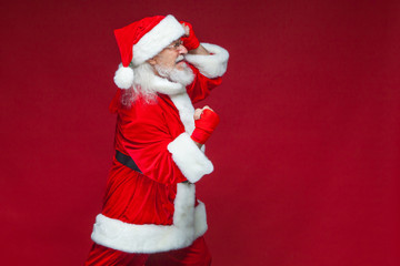 Christmas. Santa Claus with red bandages wound on his hands for boxing imitates kicks. Kickboxing, karate, boxing. Isolated on red background.