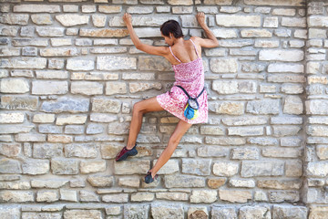 A woman in a dress is climbing a brick wall.
