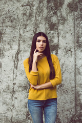 Maybe you? Beautiful young woman looking at camera while standing against concrete background outdoors 