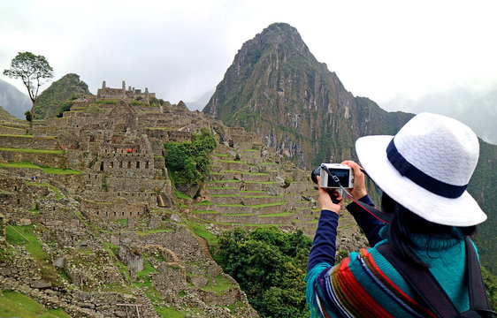 One female tourist taking picture of the Inca ruins in Machu Picchu, the famous archaeological site in Cusco region of Peru
