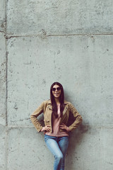 Candid style. Full length of beautiful young woman looking at camera with smile while standing against concrete background outdoors 