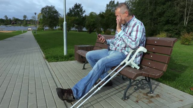 Cheerful man with crutches in a park on a bench