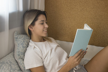 Happy girl reading a paper book, lying on a bed