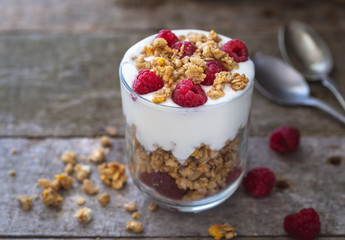 Yogurt with muesli in glass bowl with pieces raspberries on top.