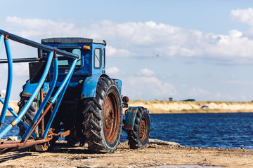 old tractor with trailer stands on shore of sea bay.