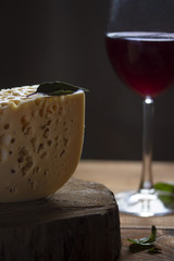 one whole large piece of cheese with wine on a dark background