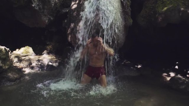 The athlete stands under a waterfall and takes water treatments. Nature landscape. Peaceful scene.