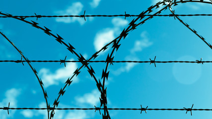 Barbed wire against blue sky and clouds.