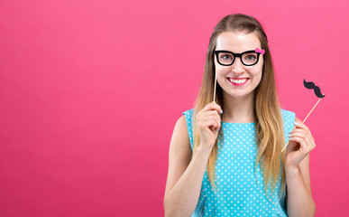 Young woman holding paper glasses and mustache party sticks on a pink background