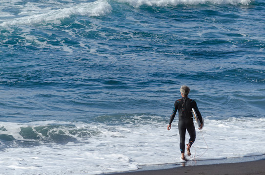 Hombre entrando al mar para hacer surf durante el atardecer en en la playa de El Socorro, Los Realejos. Isla de Tenerife, Islas Canarias. España.