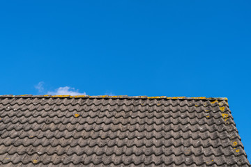 Roof with grey roof tiles and a clear blue sky with some clouds on a sunny day