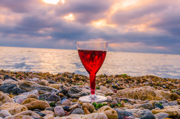 Glass with wine on the sea beach during the sunset