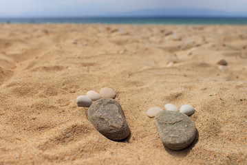 Foot prints made of pebbles stones on golden beach sand