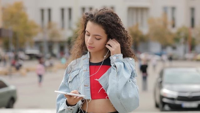 Portrait of young multiracial girl puts on earphones in urban city square