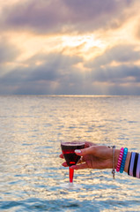 Girl holding a glass with wine uring the sunset on the sea