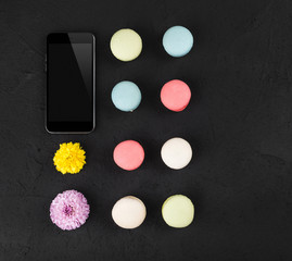 Composition with colorful macarons, flowers and mobile phone on black stone table. Top view, flat lay