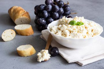 Organic ricotta cheese in white bowl with grapes and baguette.