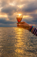 Girl holding a glass with wine uring the sunset on the sea