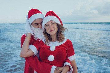 Obraz premium Happy couple walking on the beach in Santa Claus costumes. The concept of vacation for Christmas.