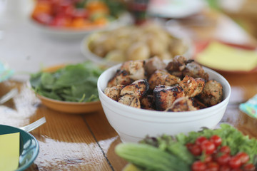 Dish with shish kebab among plates with vegetables and potatoes on a wooden table