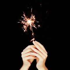 Beautiful woman hands holding sparkler lights in front of black, can be used as background 