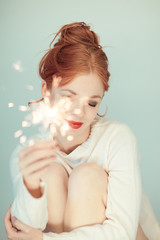 Beautiful woman with red hair holding sparkler lights, cozy, bright winter sweater, can be used as background