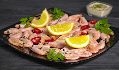 Fototapeta na wymiar sauce and shrimp with pepper, lemon and greens on a black plate