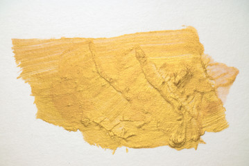 smear of gold metallic paint on white paper with texture