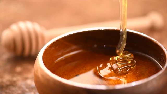 Honey pouring in wooden bowl. Honey closeup. Healthy organic thick honey dipping from the wooden honey spoon. Slow motion. 3840X2160 4K UHD video footage