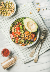 Vegan lunch bowl. Flat-lay of vegan dinner with avocado, mixed grains, beans, sprouts, greens and vegetables with salt and spices over marble table, top view. Vegetarian, healthy diet food concept