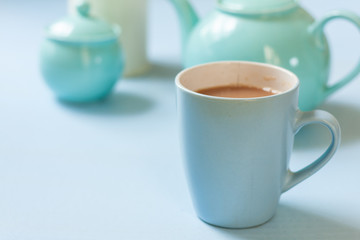 A blue mug of tea with tea pot and accessories on a pale blue background