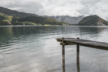 Photo of wooden deck in the cold lake in austrian Alps with hills and mountains in the background