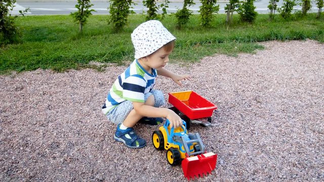 4k footage of cute toddler boy playing in park with toy loader and trailer