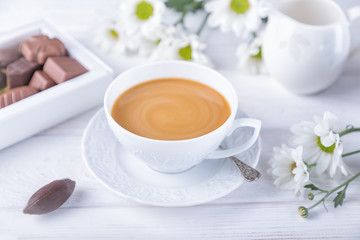 Coffee with milk, chocolate candies and chrysanthemums flowers on a white background