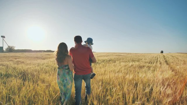 Young parents go with their son on a wheat field in the evening.